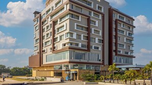 Ein mehrstöckiges Hotel mit modernem architektonischen Design, das eine Mischung aus rechteckigen und quadratischen Fenstern, einen markanten Eingang mit Glasfassade und eine angelegte Fläche mit Palmen bietet.