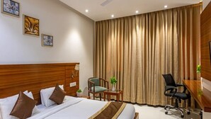 Ein Hotelzimmer mit hölzernem Kopfteil, einem Bett mit braunen Kissen, einem Schreibtisch mit Stuhl und einem großen Fenster mit Vorhängen.