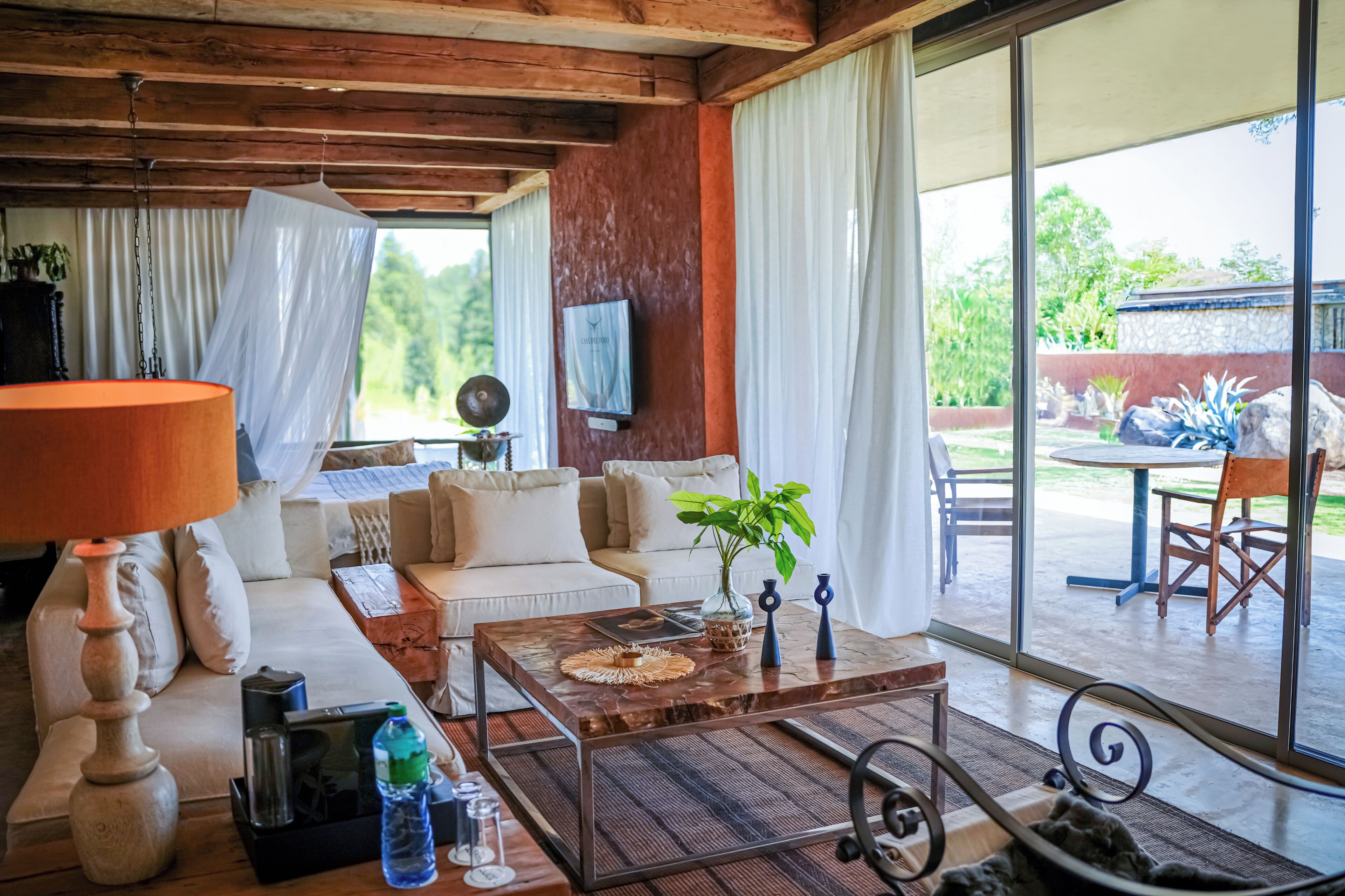 A living room with a sofa, coffee table, lamp, and a view of the outdoors.