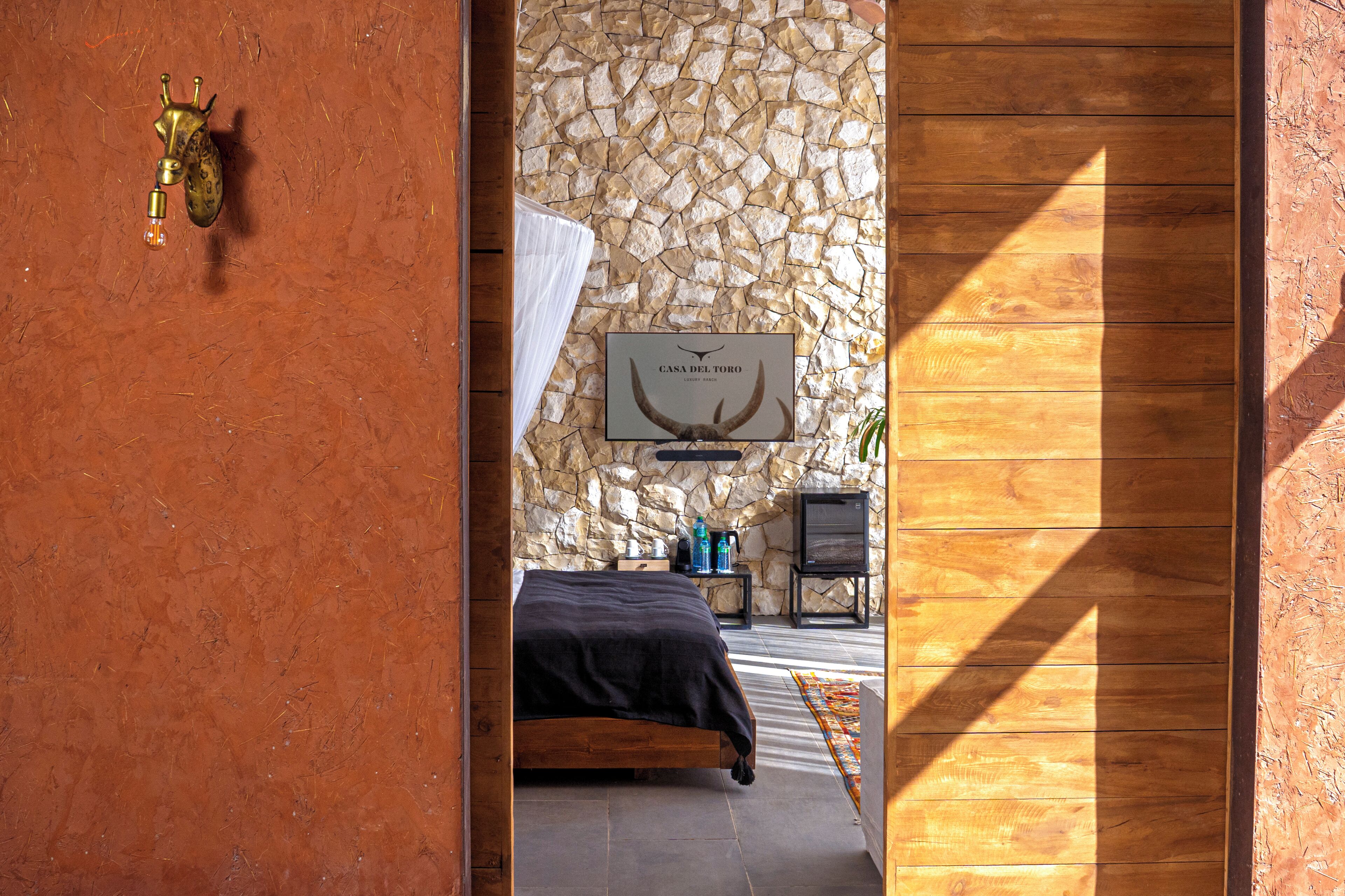 Una habitación con pared de piedra, una cama, un televisor y una puerta de madera.