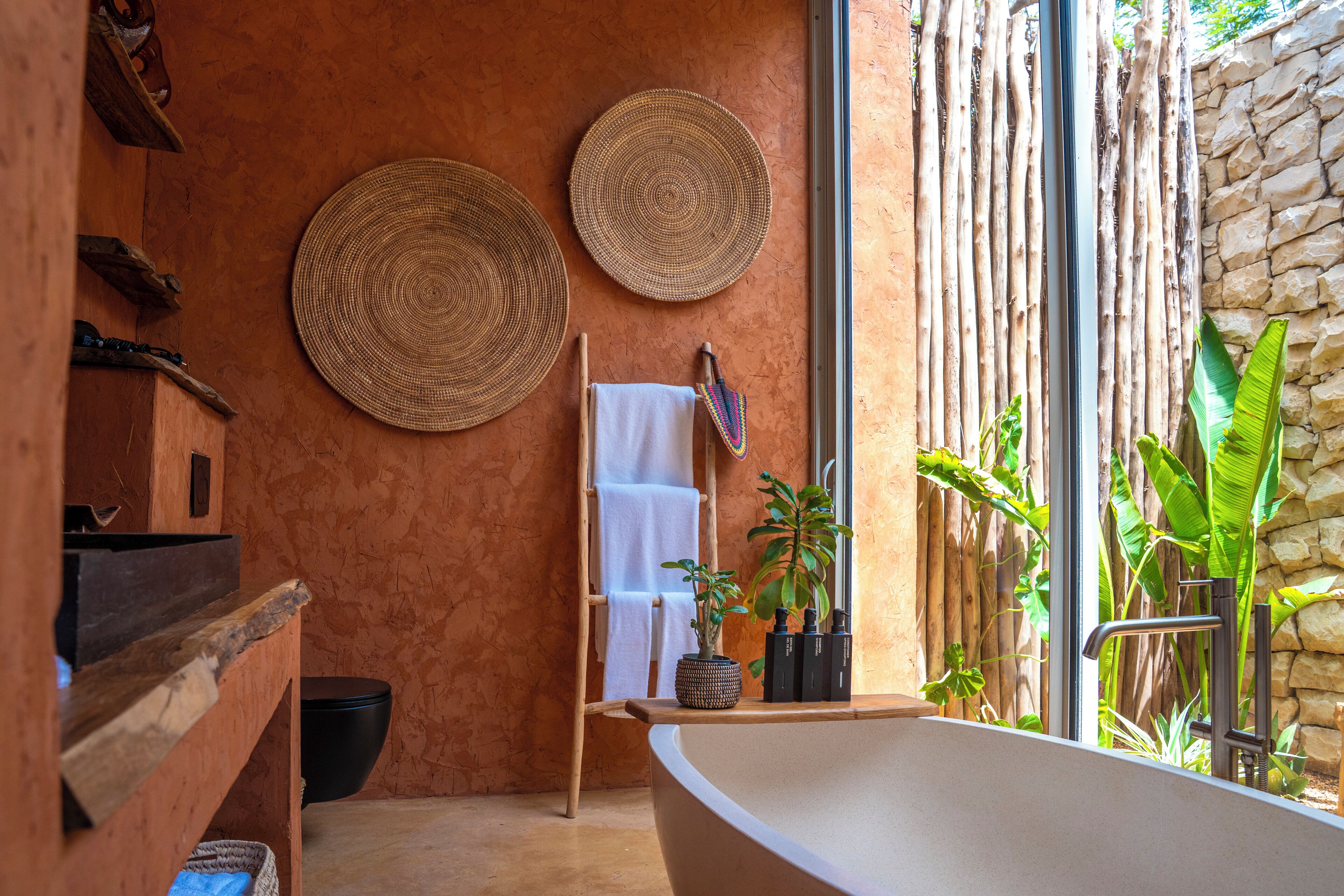A bathroom with a bathtub, woven mats, a towel rack, and a potted plant.