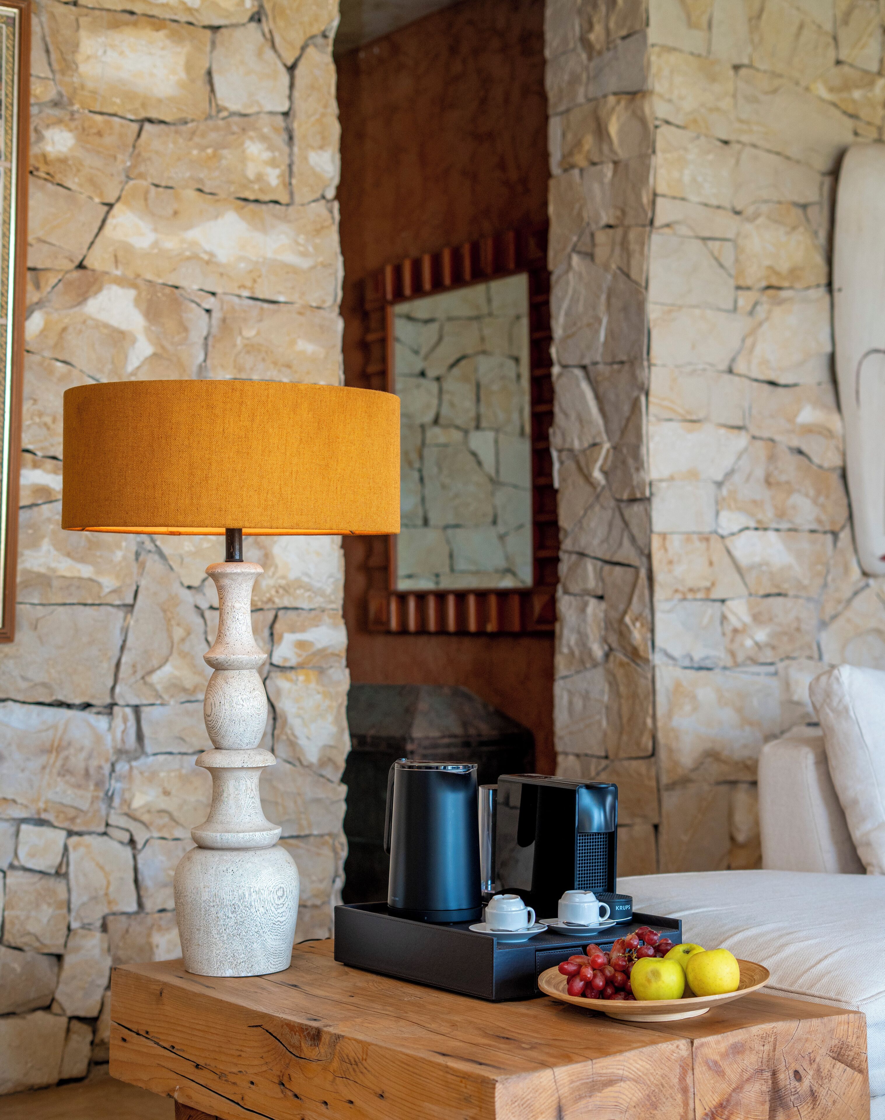 A wooden table with a lamp, coffee maker, and a fruit bowl.
