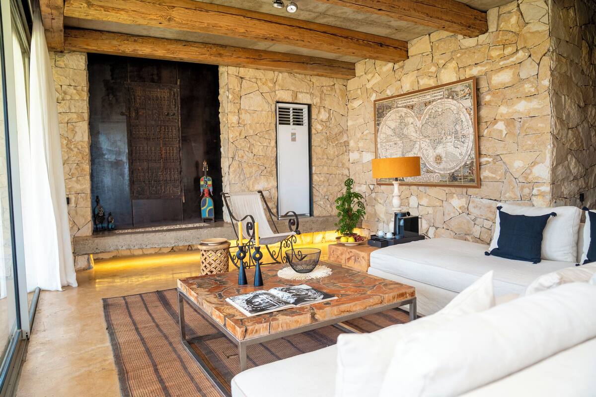 Uma sala de estar com paredes de pedra, uma lareira, um sofá, uma mesa de centro com revistas e um mapa na parede.