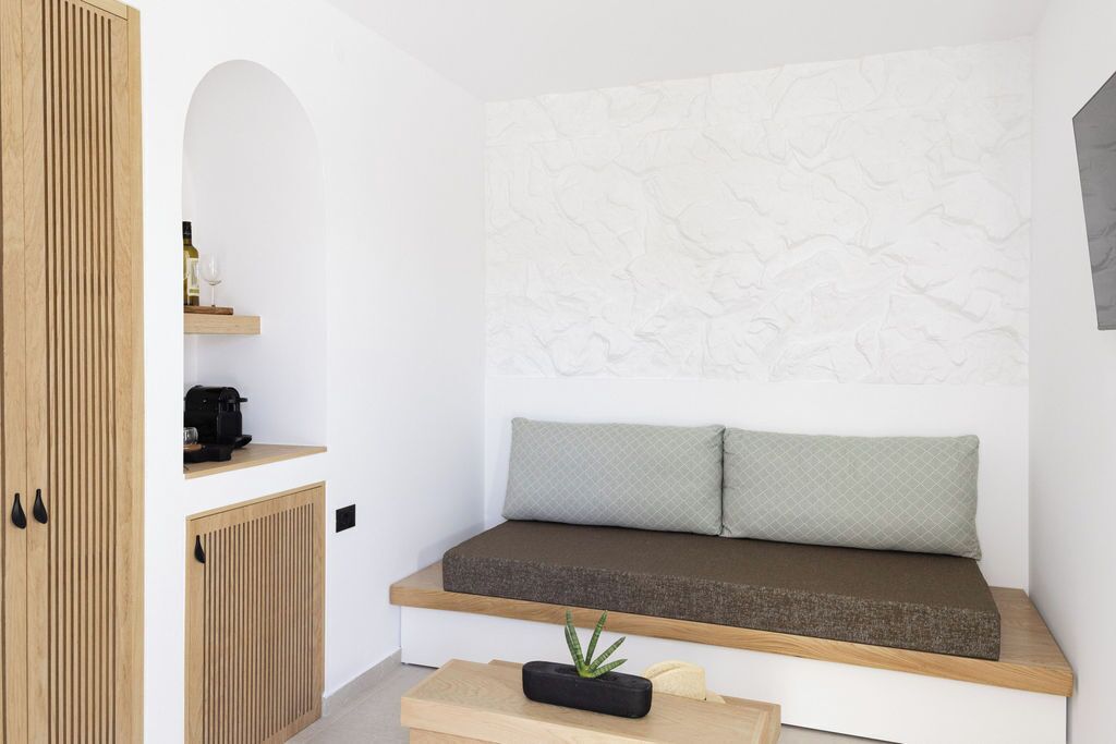 A compact room with a built-in bench, a small shelf with a bottle and a glass, and a plant on a table.