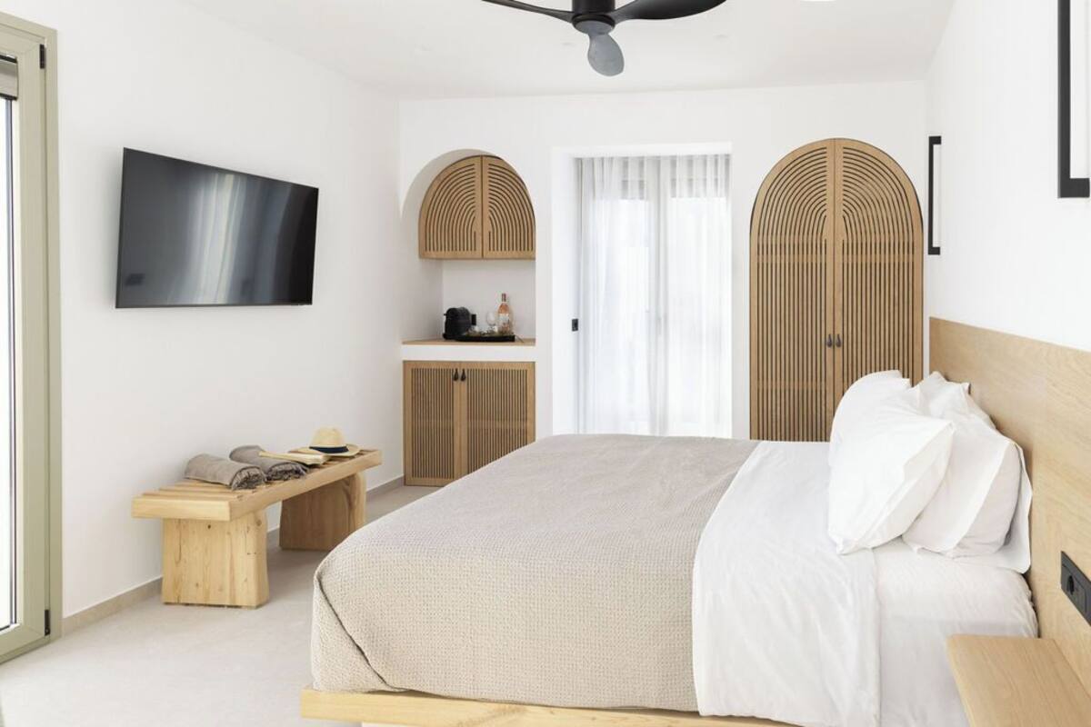 Ein modernes Schlafzimmer mit Bett, Fernseher, einer Holzbank und einem Kleiderschrank.