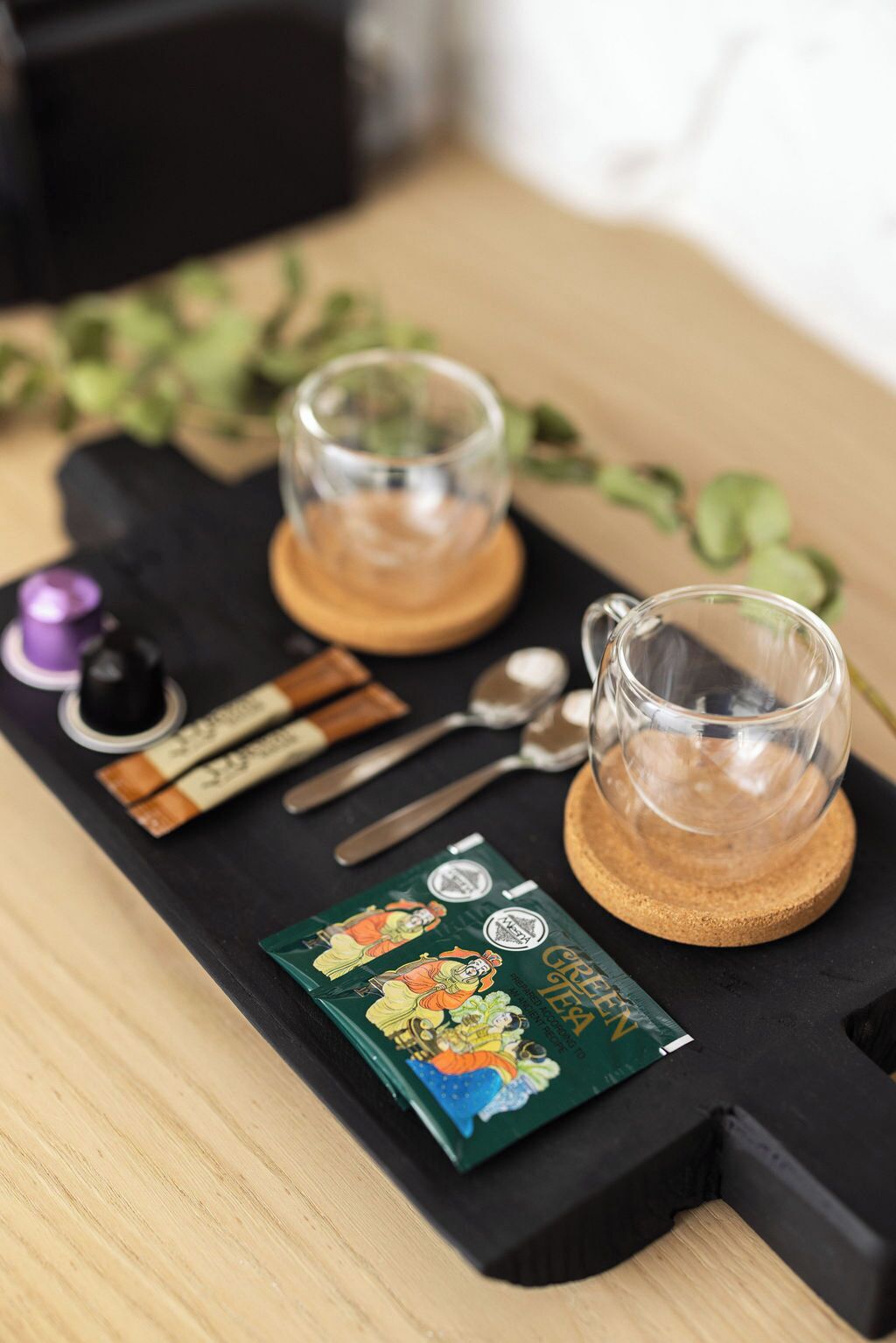A tray with two glasses of a clear liquid, a small pitcher, a spoon, a knife, and two packets of a green tea product.