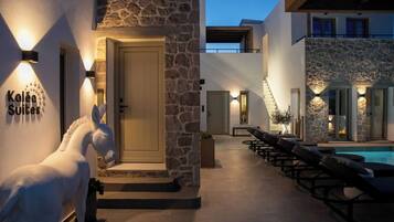 A modern hotel exterior with stone walls, a pool area, and lounge chairs.
