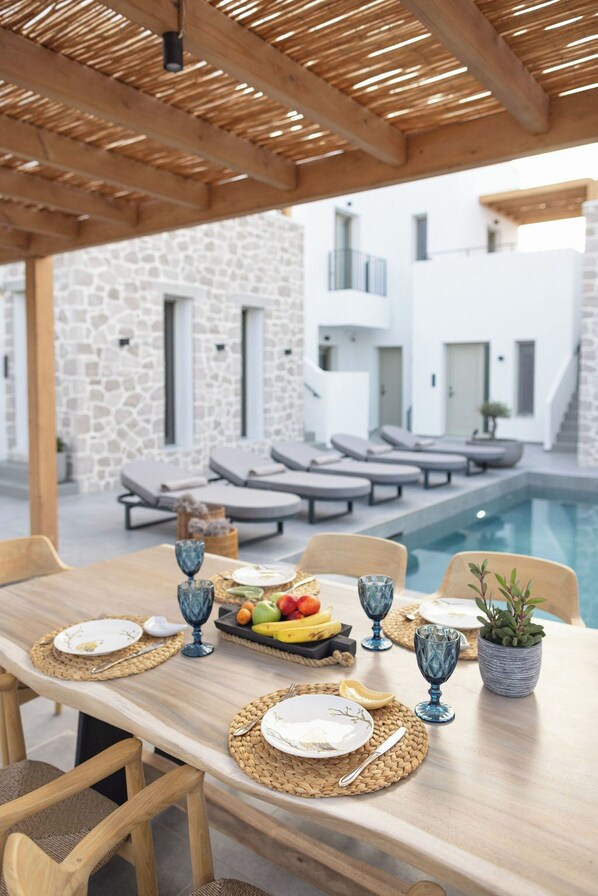 Area pranzo all'aperto con piscina, pareti in pietra e poltrona relax.