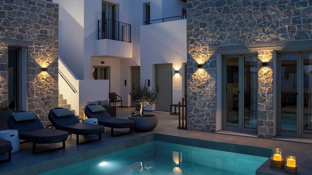 A modern pool area with stone walls, lounge chairs, and a staircase leading to an upper level. - Kalea Suites (Milos)