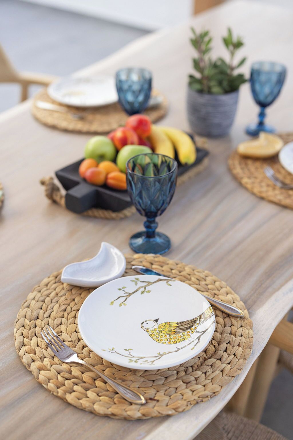 Una mesa de comedor dispuesta con individuales, platos, cubiertos y un frutero.