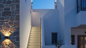 A modern building with a stone wall, a staircase, and a balcony. - Kalea Suites (Milos)