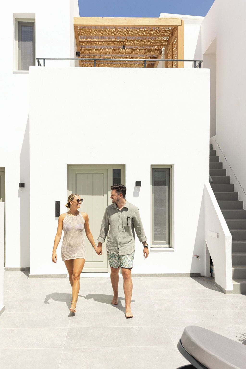 A modern white building with a wooden pergola, a staircase, and a door.