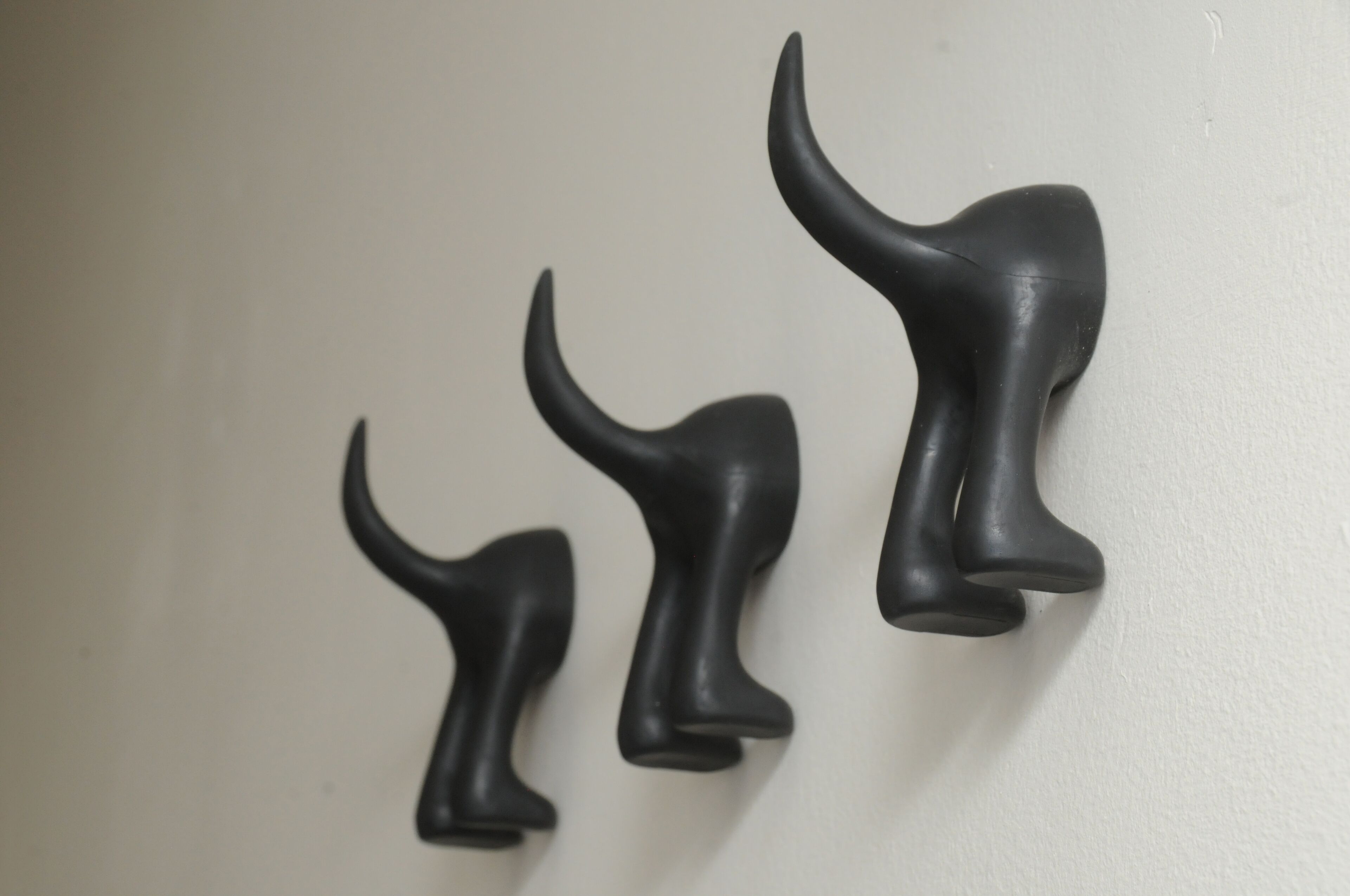 Three black wall-mounted hooks of varying sizes.