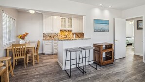 A modern kitchen with white cabinets, a marble countertop, and a dining area with wooden furniture.