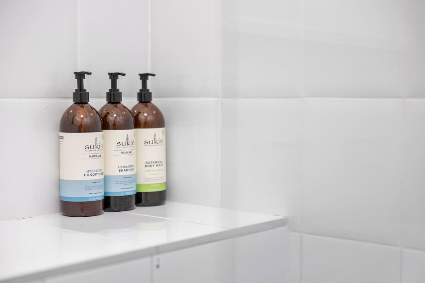 Three bottles of Sukin haircare products on a white shelf in a bathroom.