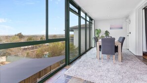Un balcon avec vue sur la campagne, un coin repas avec une table et des chaises, et une grande fenêtre.