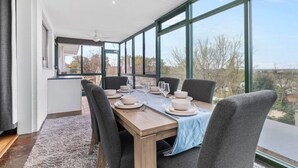 Un coin repas avec une table dressée pour quatre personnes, de grandes fenêtres et une vue sur l’extérieur.