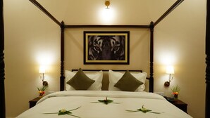 A four-poster bed with a tiger-themed artwork above it, two bedside lamps, and decorative floral arrangements on the bed.