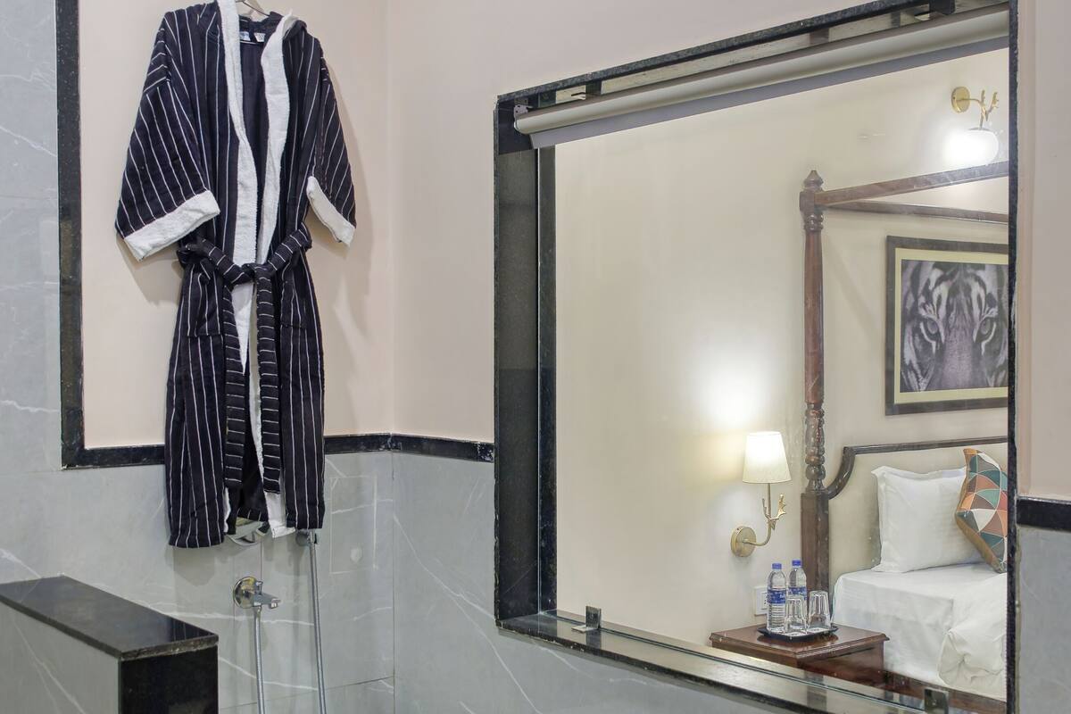 A bathroom with a bathtub, a large mirror, a robe hanging, and towels on the counter.