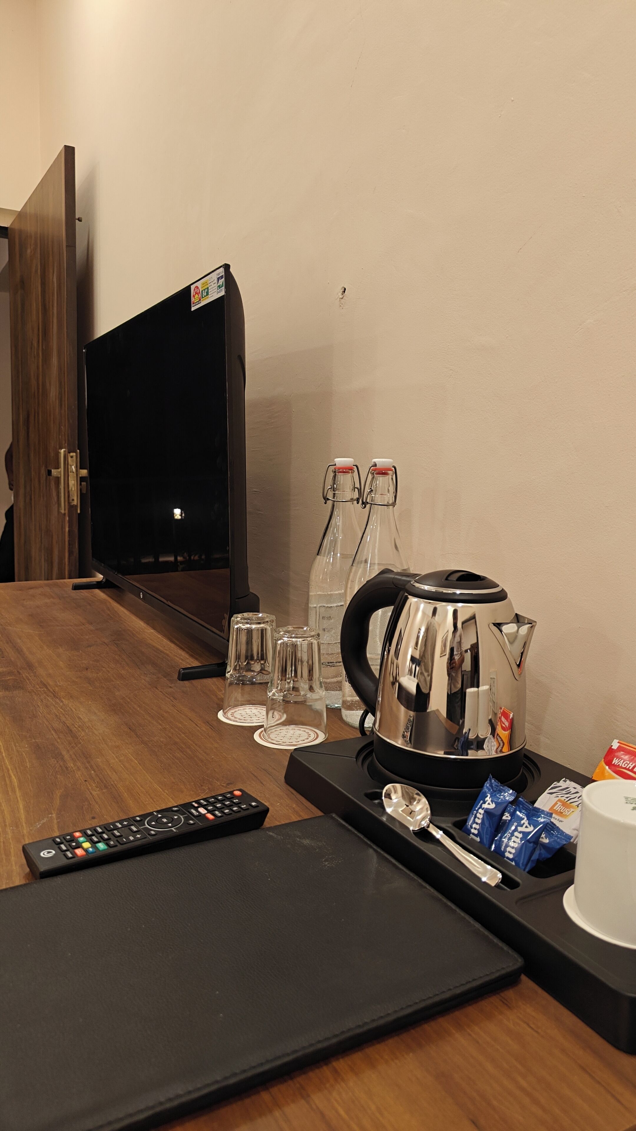 Habitación de hotel con una mesa de madera, una tetera, un control remoto y un pastel en una bandeja.