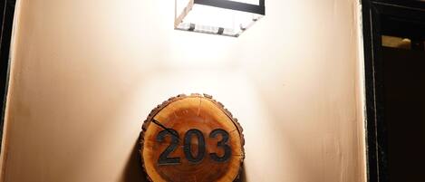 Un luminaire fixé au mur, au-dessus d’une plaque en bois portant le numéro « 203 », et un interrupteur mural en dessous.