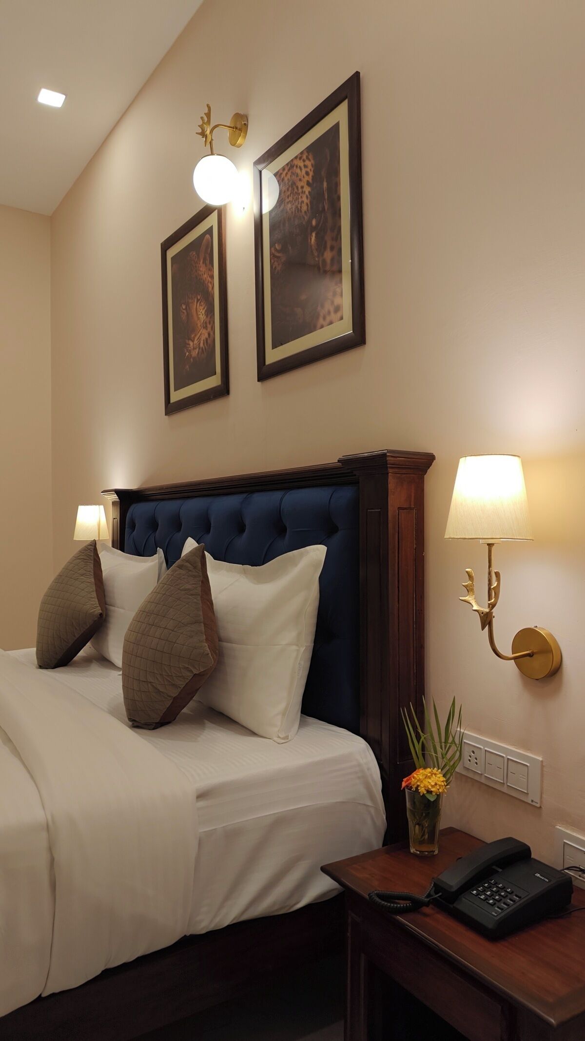 A hotel room with a large bed, two wall-mounted lamps, and framed artwork above the bed.