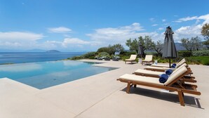 Un espace aménagé au bord de la piscine, avec des chaises longues et des parasols, offrant une vue sur une étendue d’eau et des montagnes lointaines.