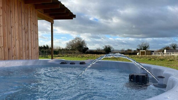 A hot tub with water flowing from a spout, surrounded by a wooden deck and a cloudy sky. - Bristol Escape Cabin With Stunning Views (Bristol)