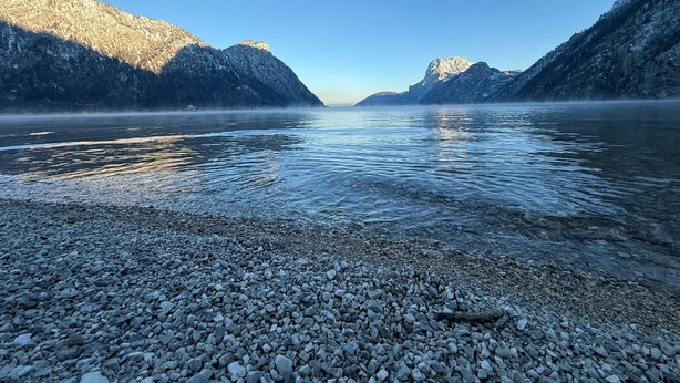 A calm lake with rocky shores and mountains in the background. - Vacation home TraunseeStrand EXKLUSIV in lakeside location incl. spacious garden (Ebensee)
