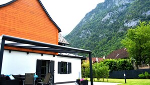 A house with a wooden roof and white walls, a patio with outdoor furniture, and a mountainous backdrop. - Vacation home TraunseeStrand EXKLUSIV in lakeside location incl. spacious garden (Ebensee)