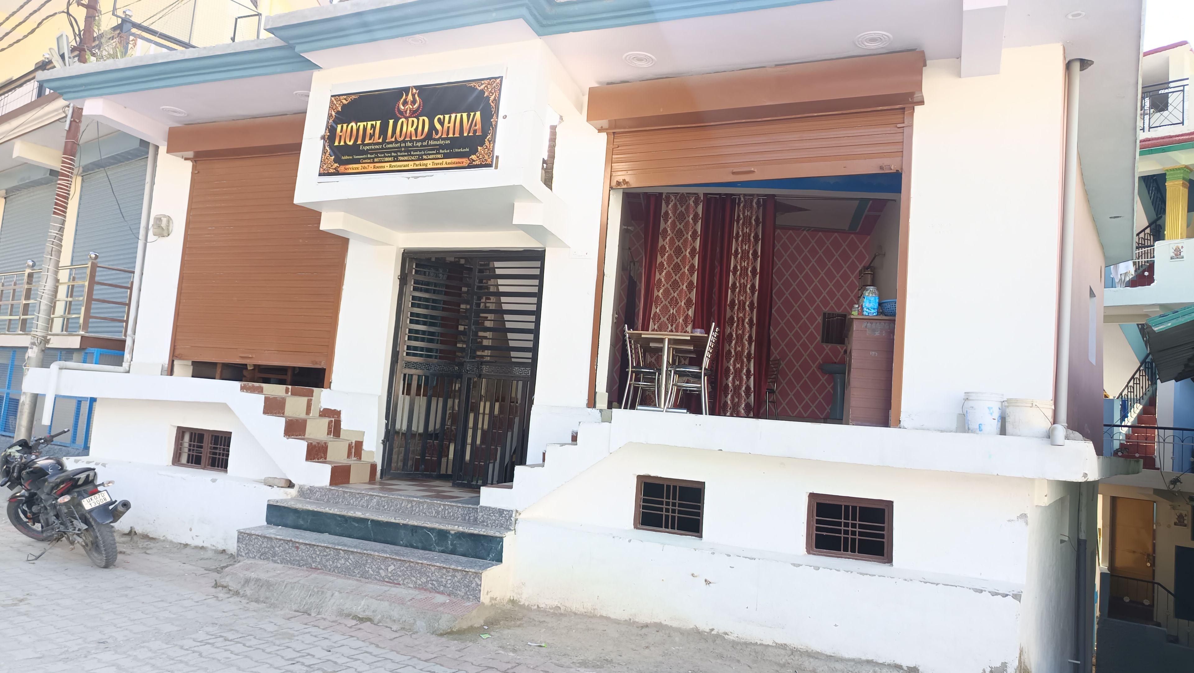 A hotel named 'Hotel Lord Shiva' with a signboard, a staircase leading to the entrance, and a motorcycle parked outside.