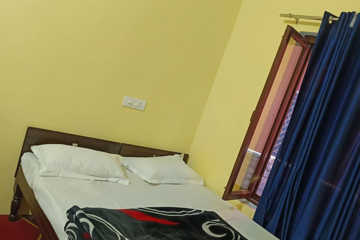 Uma cama de solteiro com manta estampada, almofadas brancas e cabeceira de madeira.