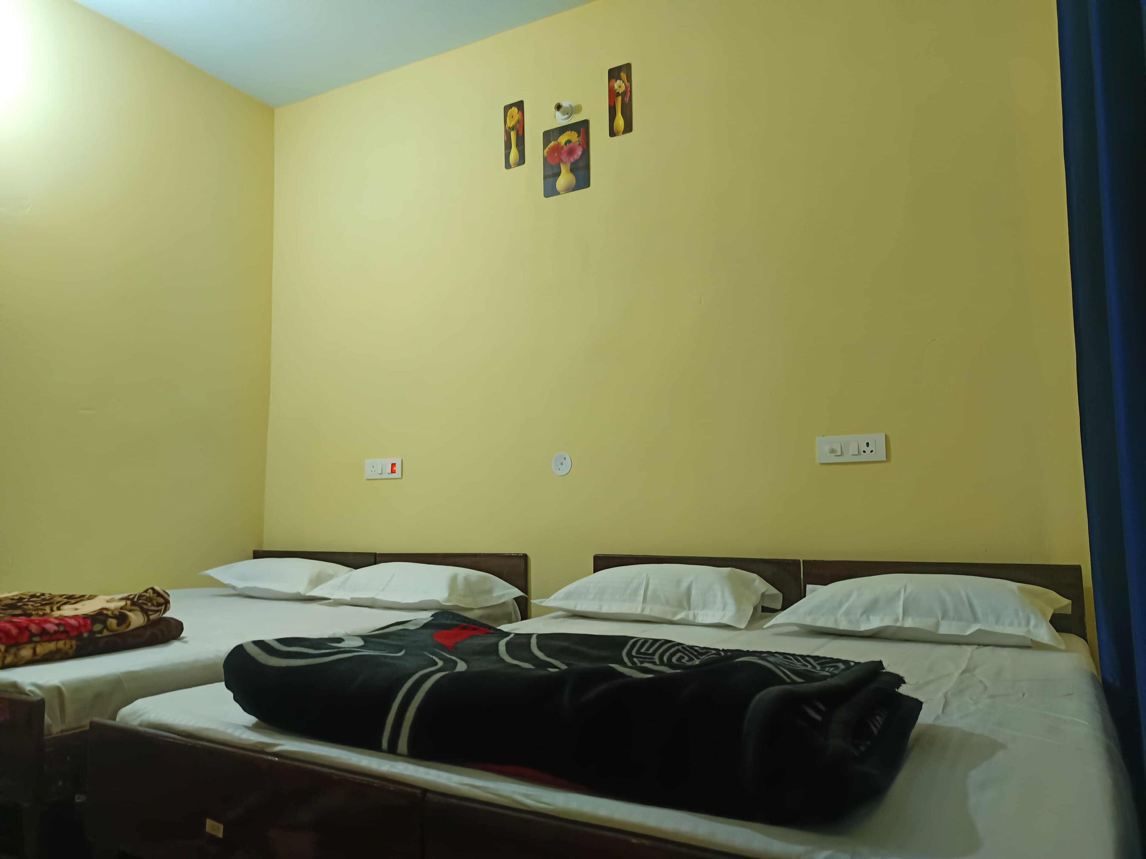 Una habitación con dos camas, cada una con almohadas blancas y una manta negra. Hay dos enchufes en la pared y un pequeño cuadro enmarcado sobre las camas.