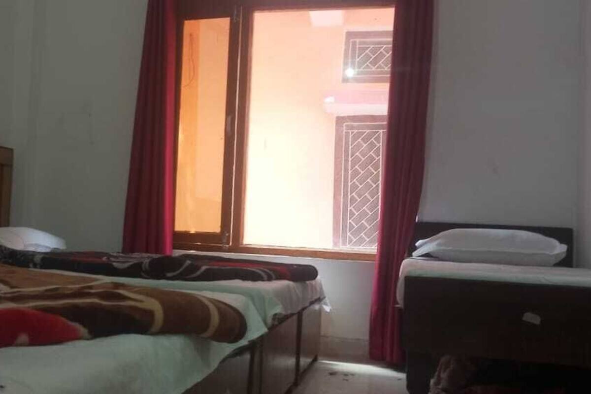 Quarto com uma cama, uma mesinha e uma janela com cortinas.