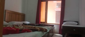 A room with a bed, a small table, and a window with curtains. - Hotel Lord Shiva (Barkot)