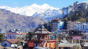 Un pueblo montañoso con un templo destacado en primer plano, rodeado de edificios residenciales y picos nevados al fondo.