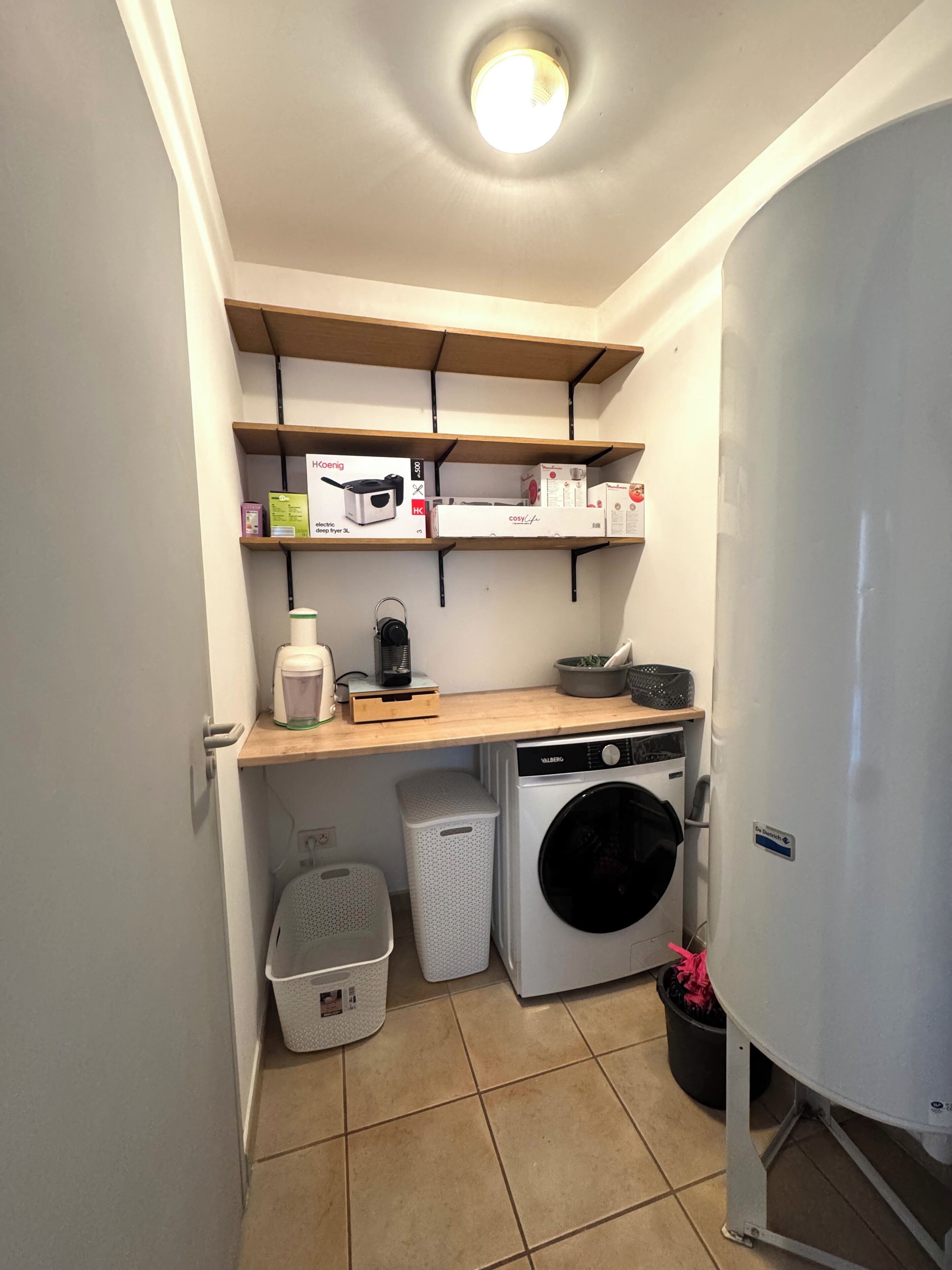 Une buanderie équipée d’un lave-linge, d’un sèche-linge, d’étagères avec des boîtes et d’une poubelle.
