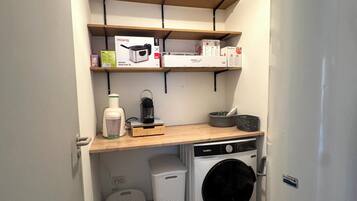 Une buanderie équipée d’un lave-linge, d’un sèche-linge, d’étagères avec des boîtes et d’une poubelle.