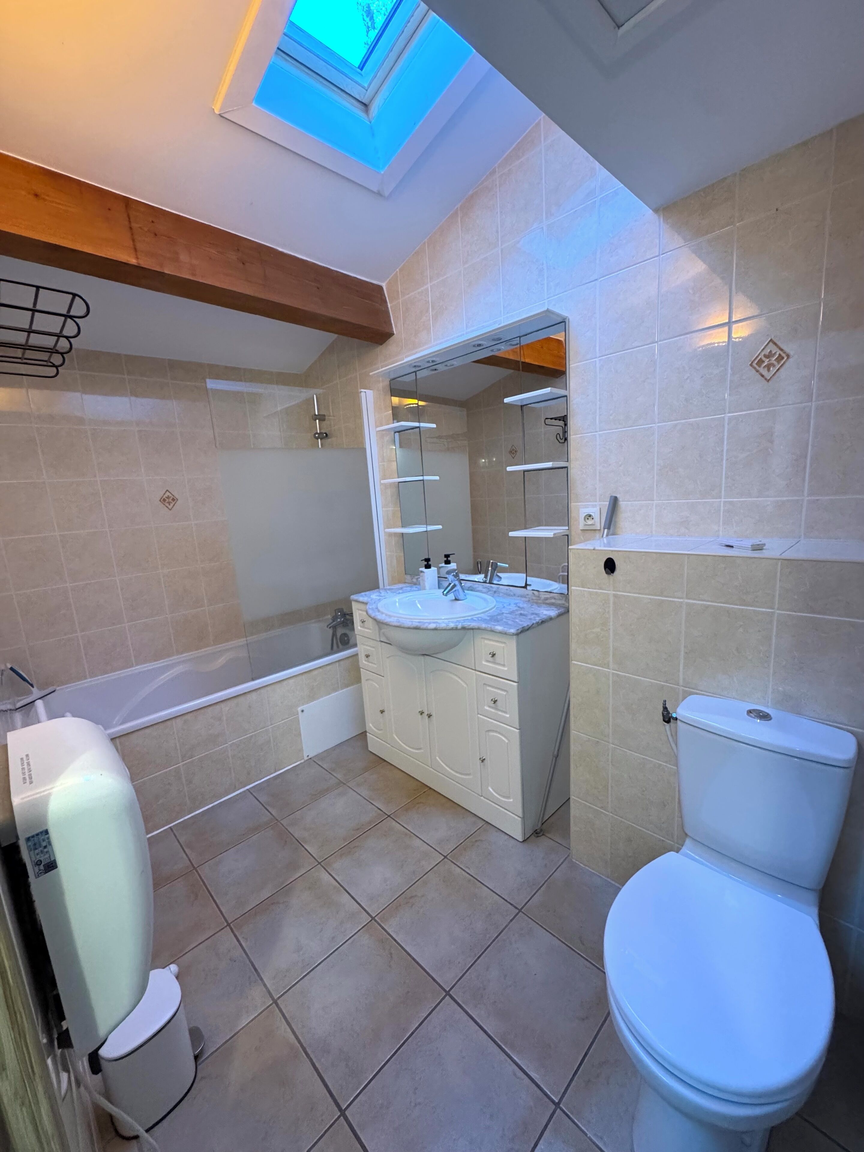 Un baño moderno con tragaluz, bañera, inodoro y tocador con lavabo y espejo.