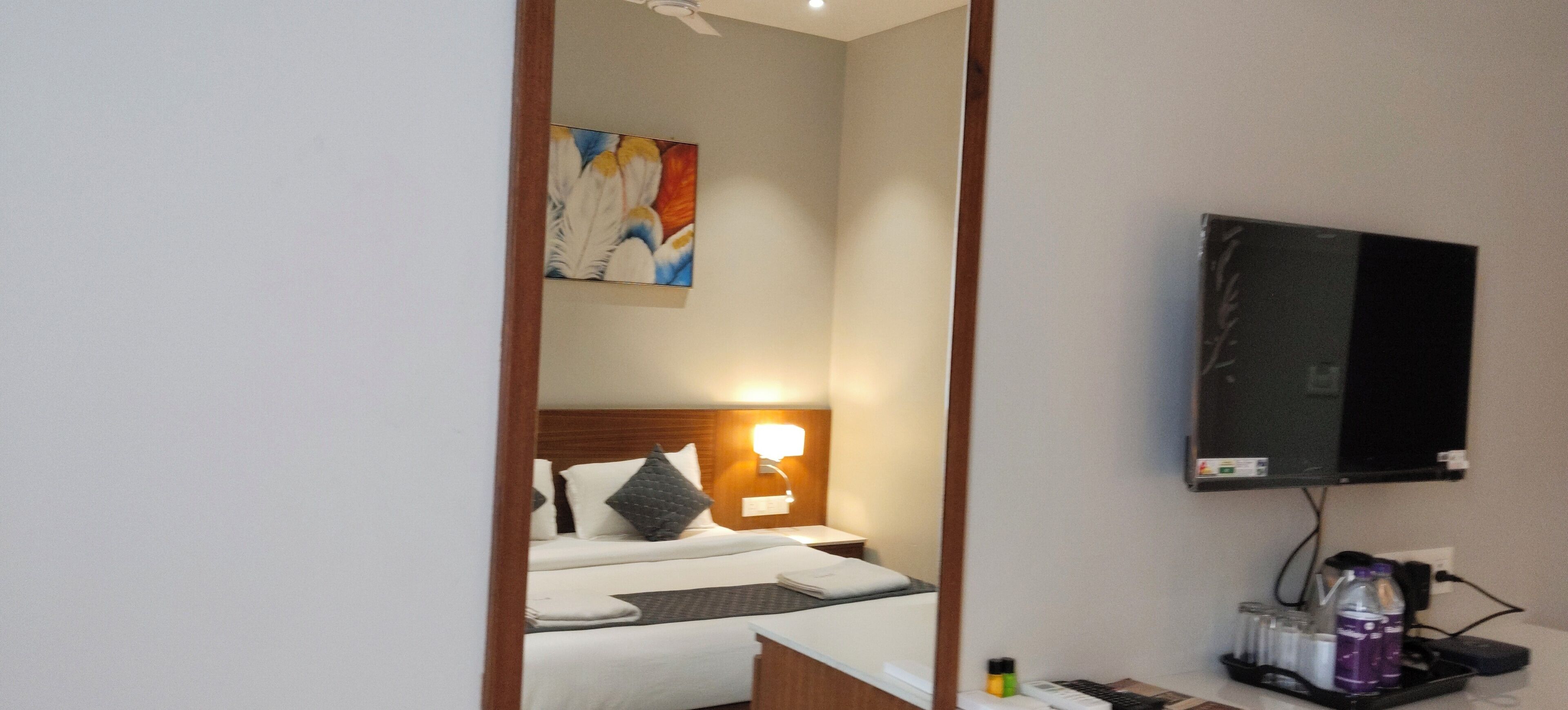 Une chambre d’hôtel avec un lit, un téléviseur fixé au mur et un tableau au-dessus du lit.