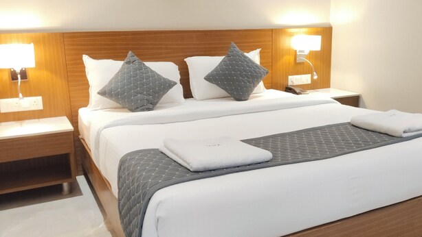 A hotel room with a large bed, two bedside tables, and wall-mounted lamps.