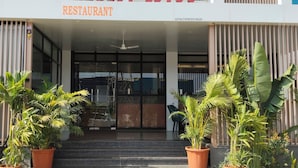 A restaurant entrance with a sign, potted plants, and an air conditioning unit.