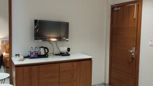 A hotel room with a wooden cabinet, a flat-screen TV mounted above it, and a wooden door.