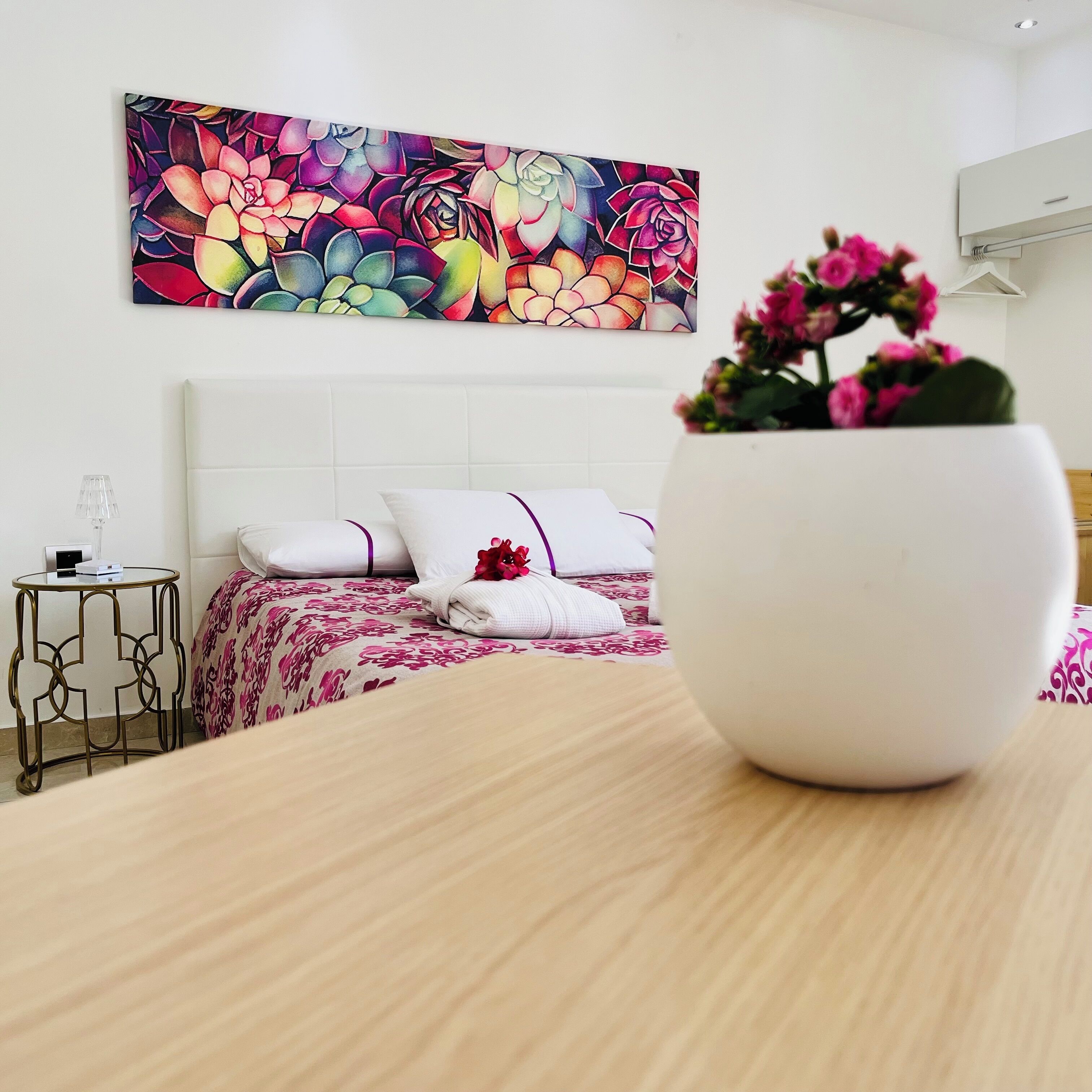A hotel room with a bed, a bedside table, a lamp, and a large floral artwork on the wall.