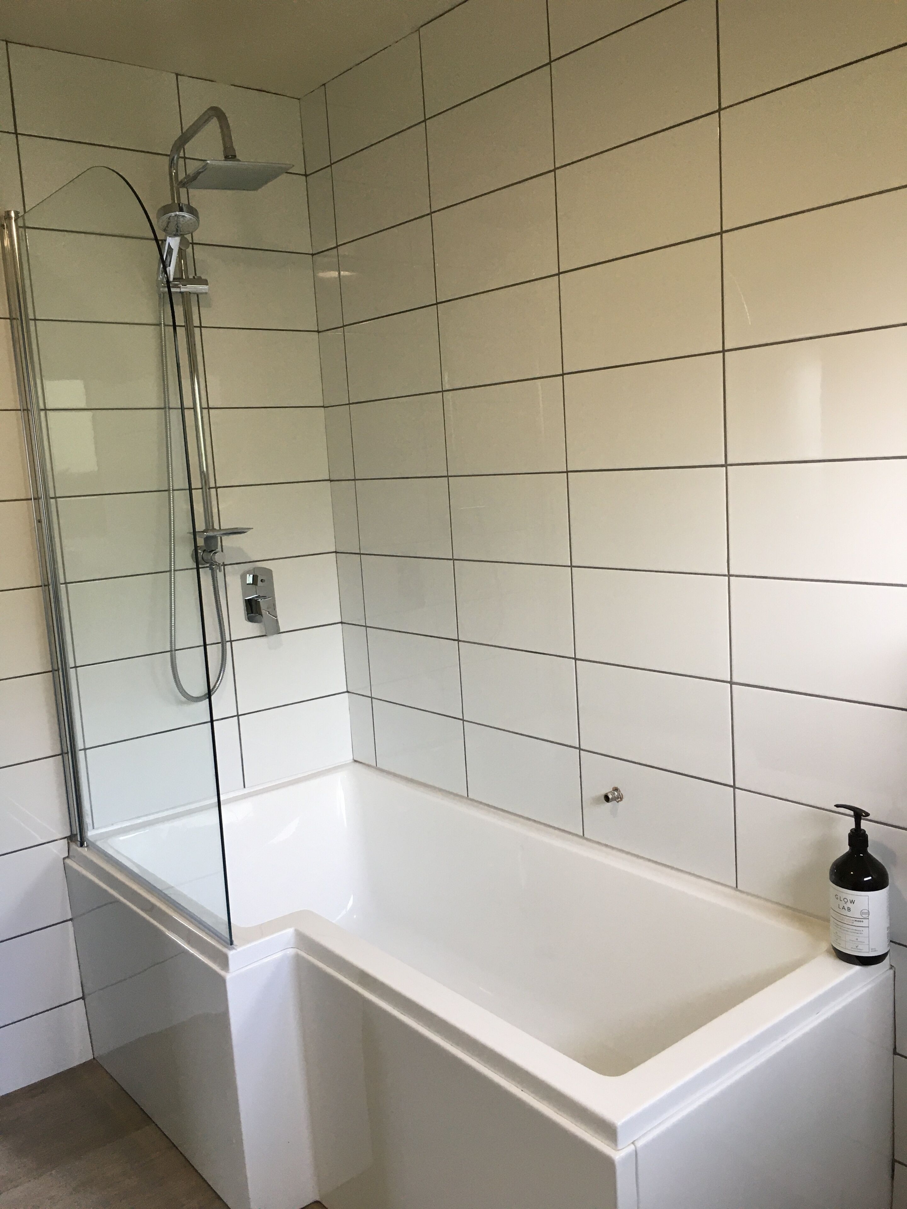 A modern bathroom with a glass-enclosed shower, a white bathtub, and a hand soap dispenser on the side.