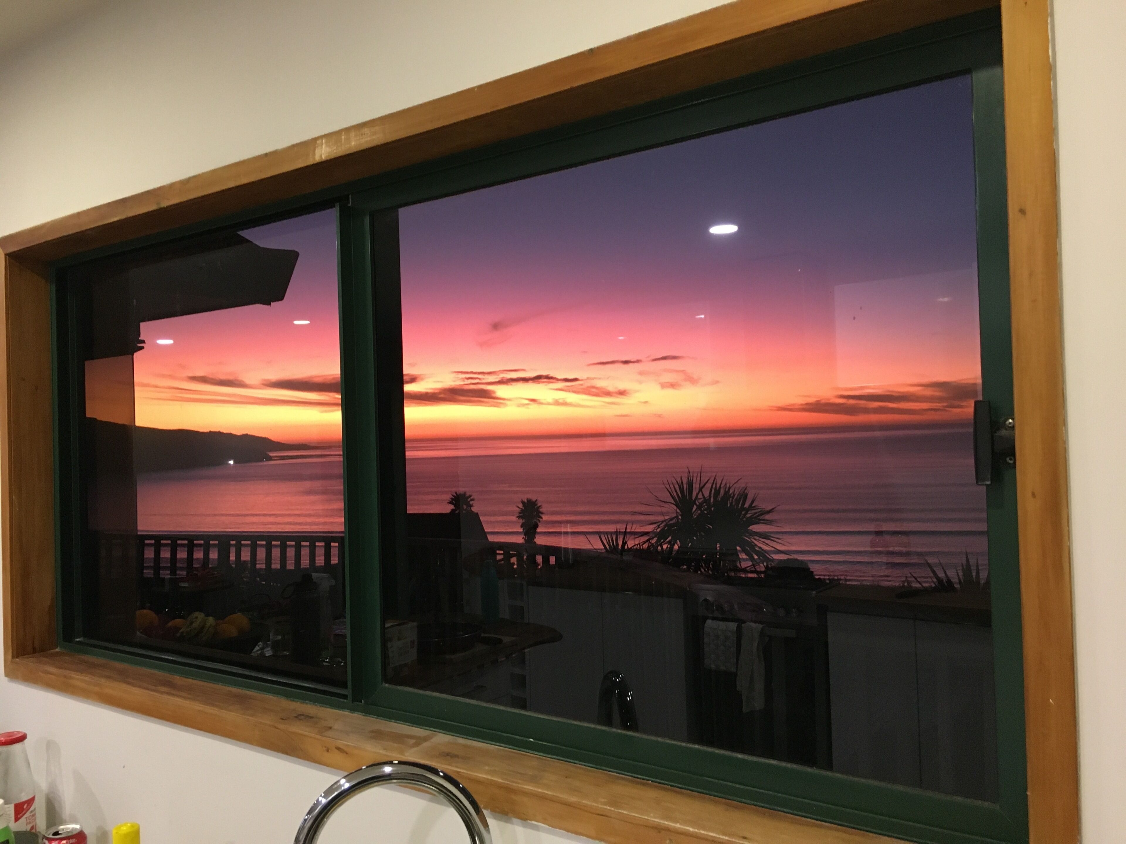 A window with a view of a sunset over the ocean, a wooden frame, and a metal handle.