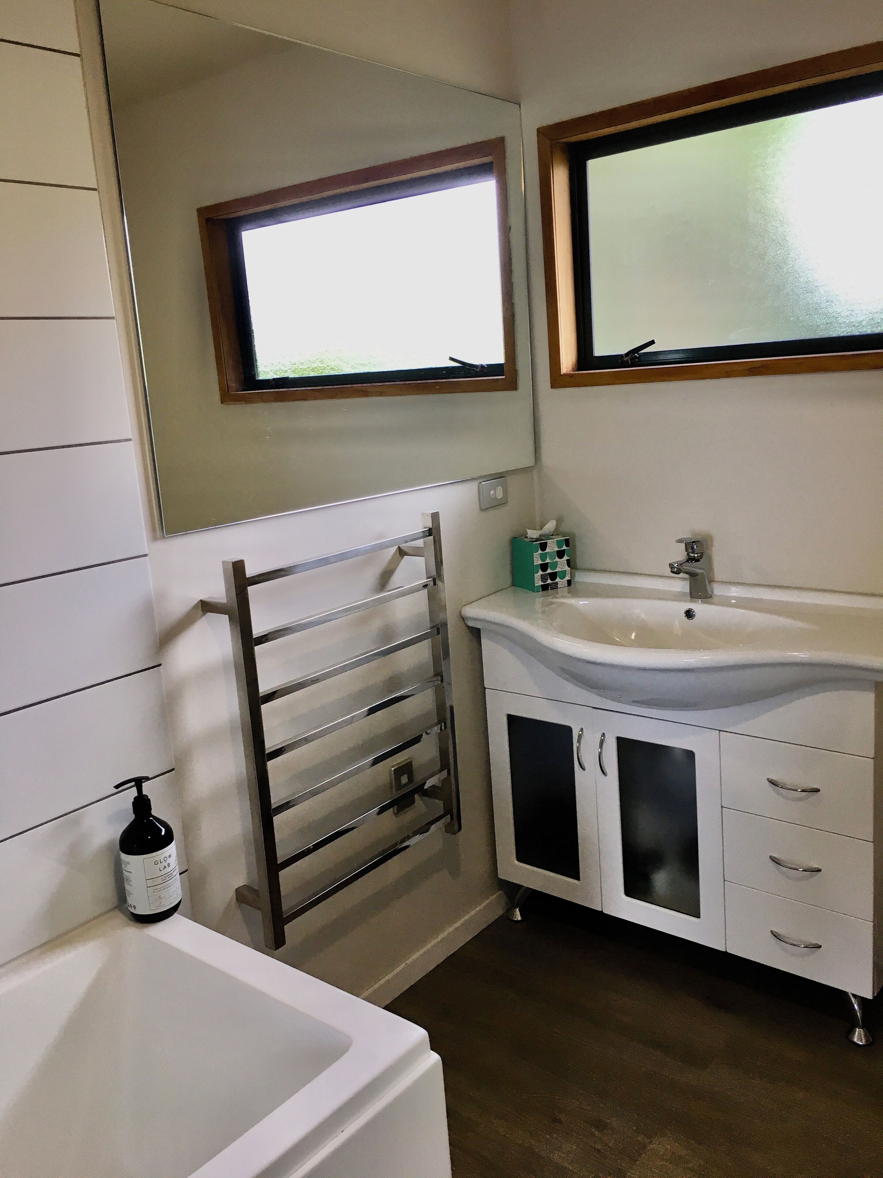 A bathroom with a white sink, a mirror above it, a window, and a towel rack.