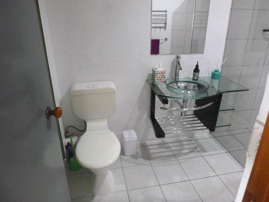 Un baño con inodoro, lavabo de vidrio, espejo y toallero.