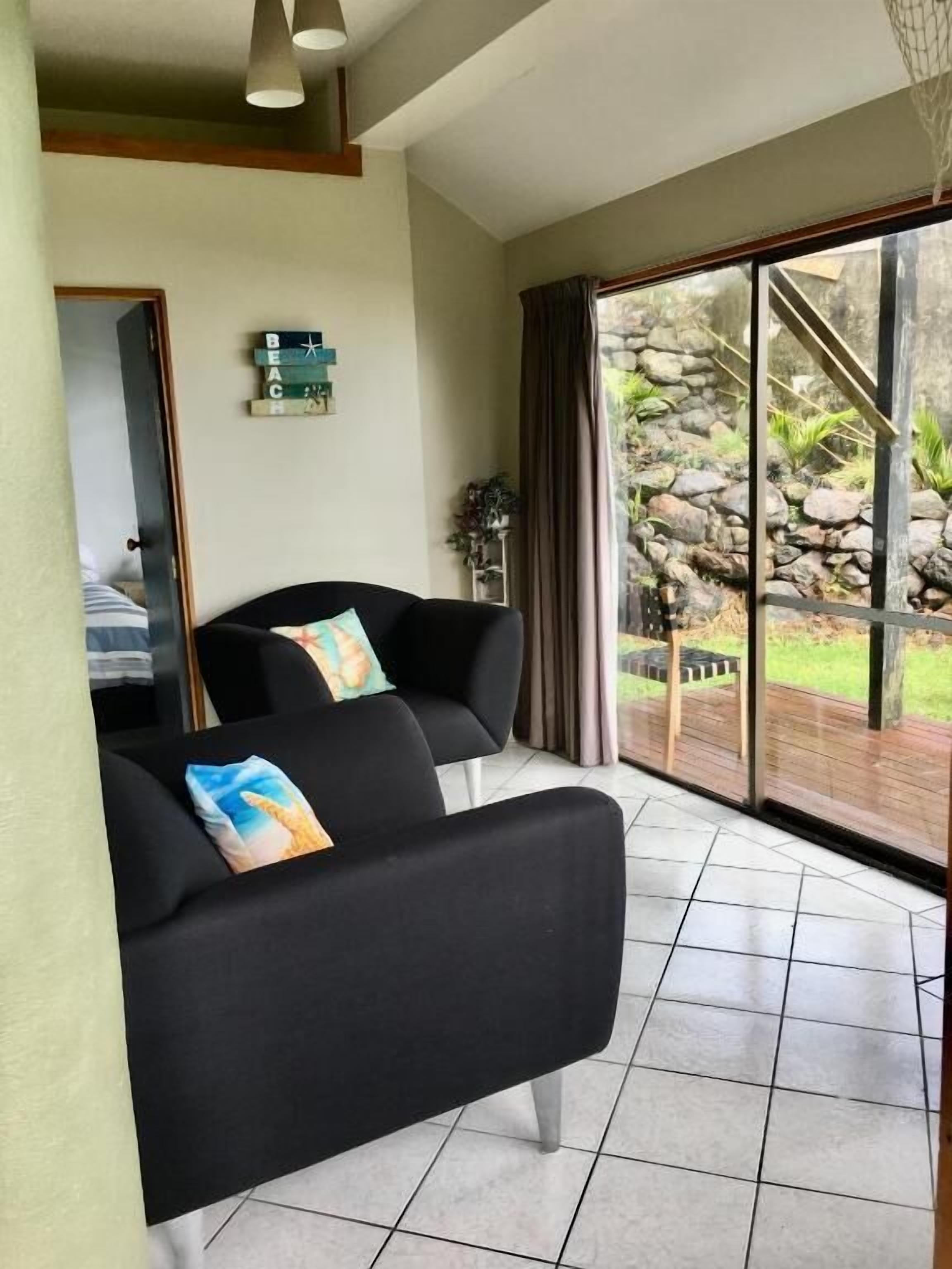 Una sala de estar moderna con un sofá negro, una mesita auxiliar y vistas a un jardín a través de amplios ventanales.