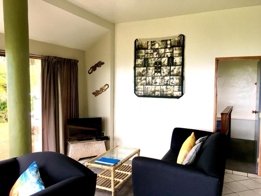 Un salón con sofá, una mesa de centro y televisor. Hay una ventana con cortinas, una obra de arte colgada en la pared y una puerta.
